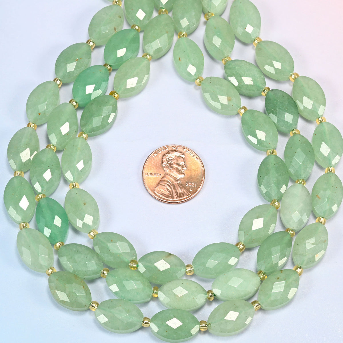 Green aventurine faceted flat oval strands formed into a teardrop loop around a US penny for scale