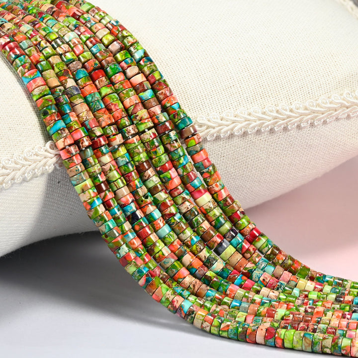 Dyed blue green sea sediment jasper heishi disc beads 2x4mm, several strands of lime green, coral orange and turquoise discs draped over a white cushion