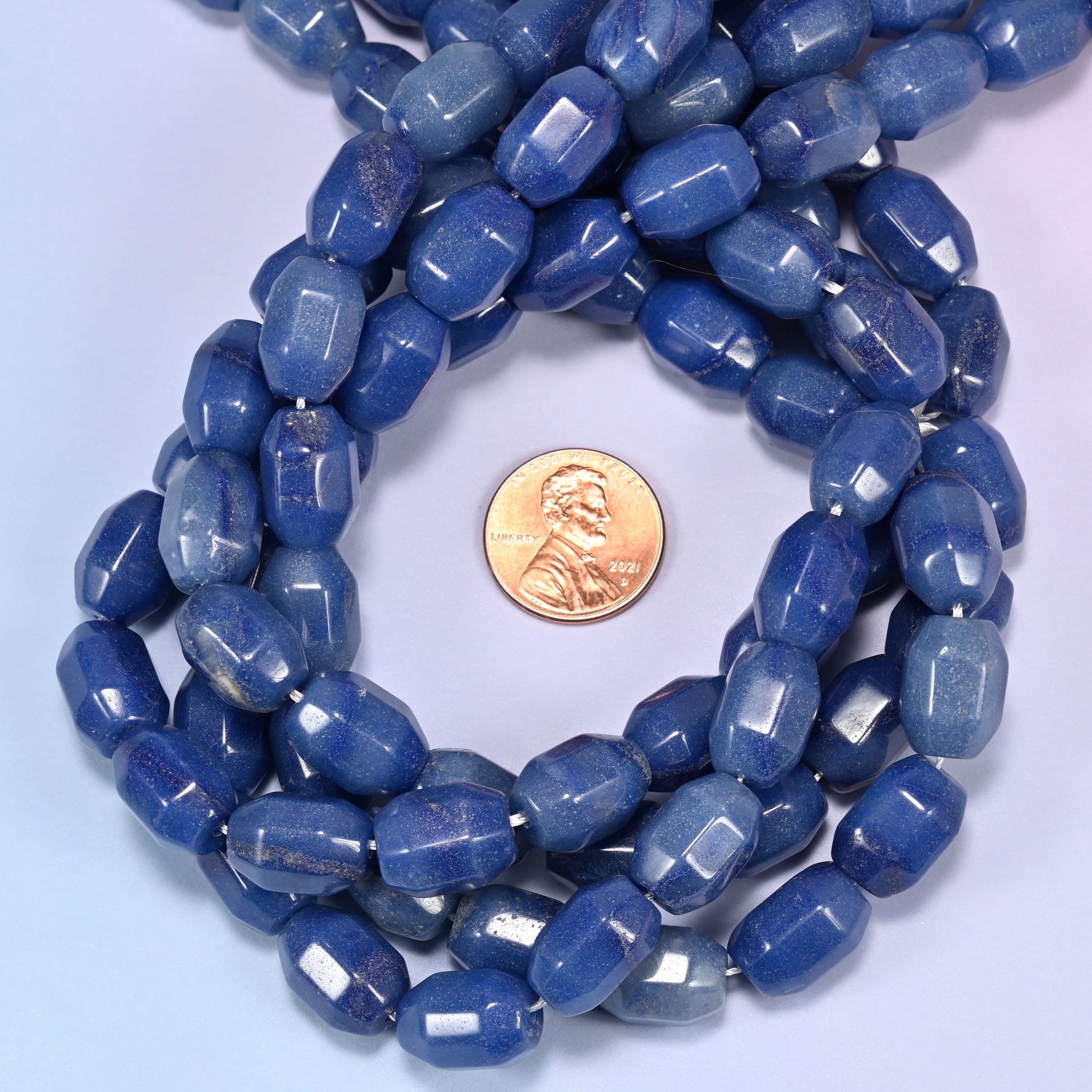 Close-up circular coil of blue faceted Aventurine barrel beads, showing the polished facets and color variation.