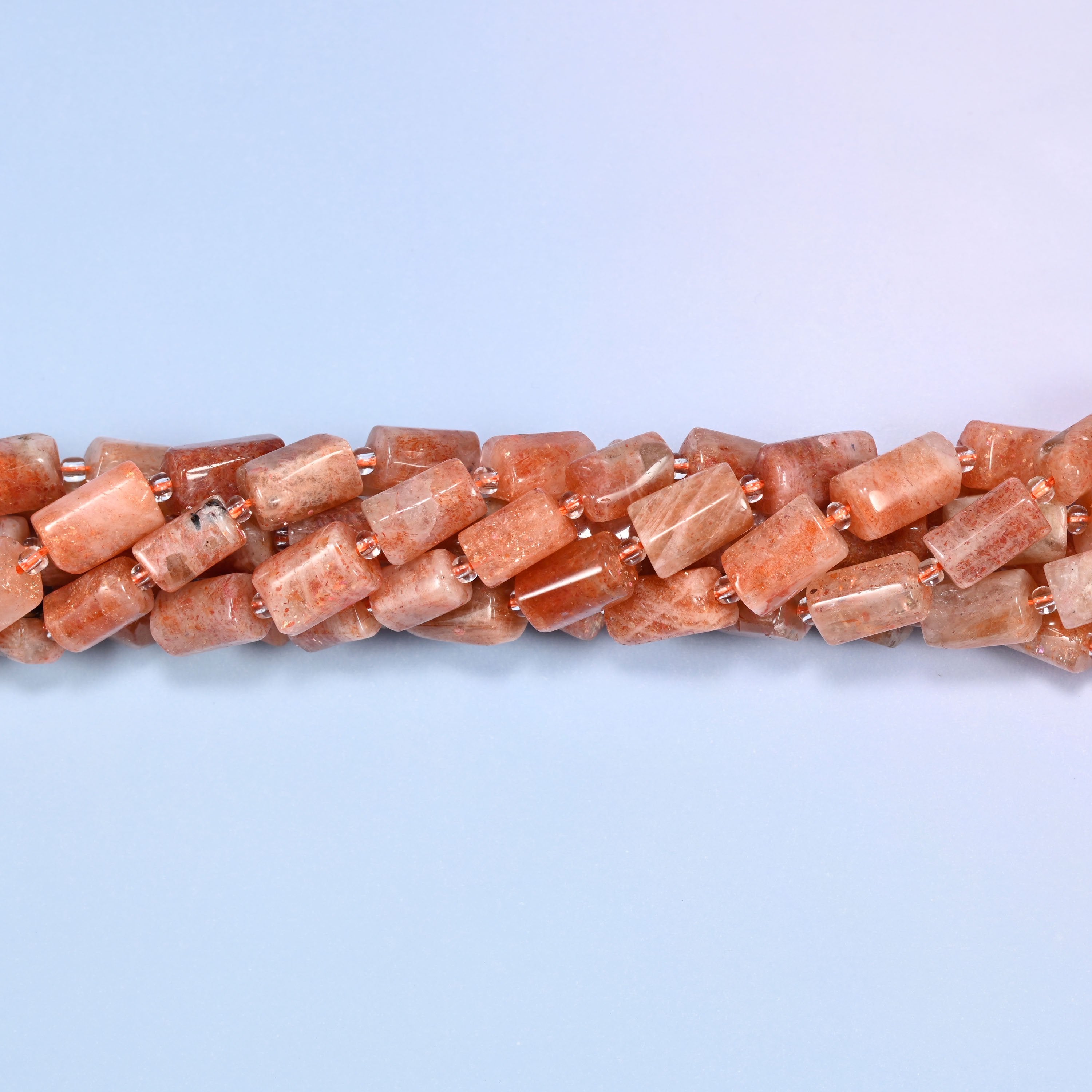 Multiple strands of faceted Golden Strawberry Quartz tube beads gathered together on a lavender surface, loose ends visible with glass spacers.