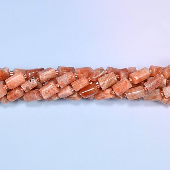Multiple strands of faceted Golden Strawberry Quartz tube beads gathered together on a lavender surface, loose ends visible with glass spacers.