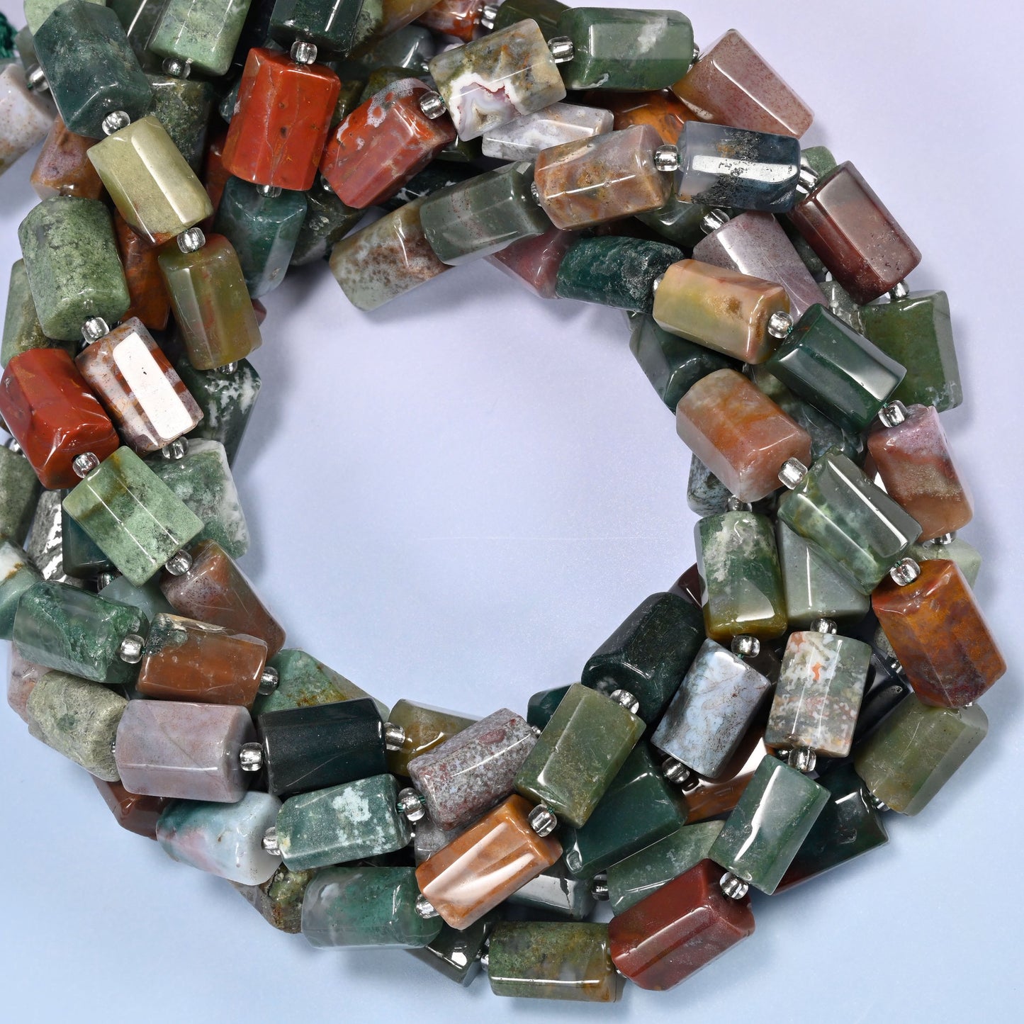 Multiple strands of faceted Indian Agate tube beads gathered into a tight loop on a lavender surface.