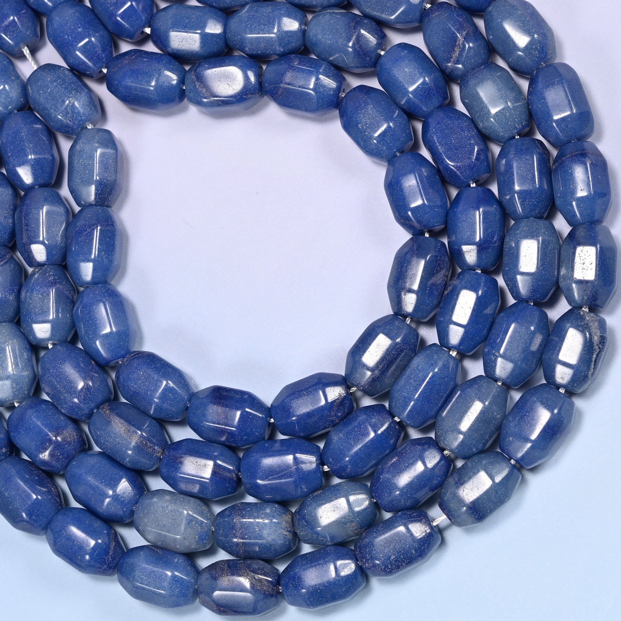 Close-up of a dense circular coil of blue faceted Aventurine barrel beads, showing the octagonal facet cuts.