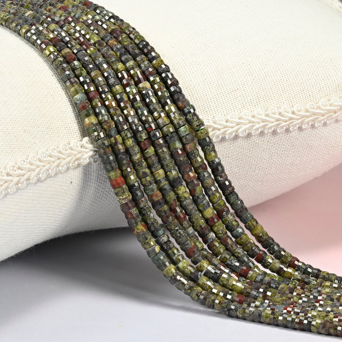 Dragon blood stone faceted heishi disc beads 2x4mm, several strands draped over a white cushion