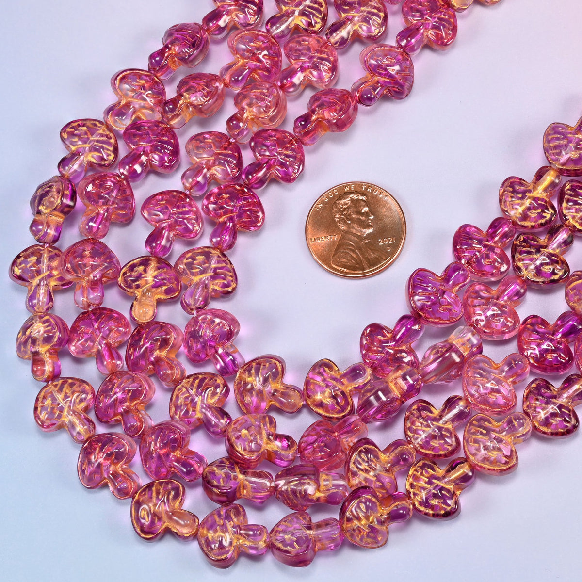 Pink gold flat mushroom glass beads laid in a wide shallow bend, magenta glass warming to gold where the wash settles into the gill lines.
