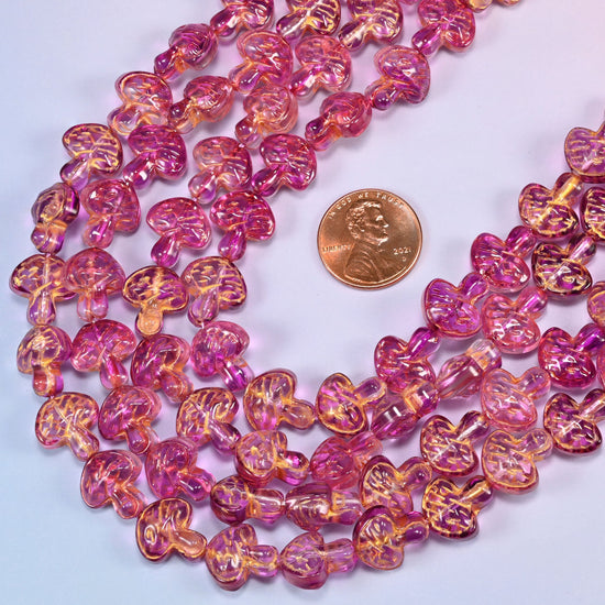Pink gold flat mushroom glass beads laid in a wide shallow bend, magenta glass warming to gold where the wash settles into the gill lines.