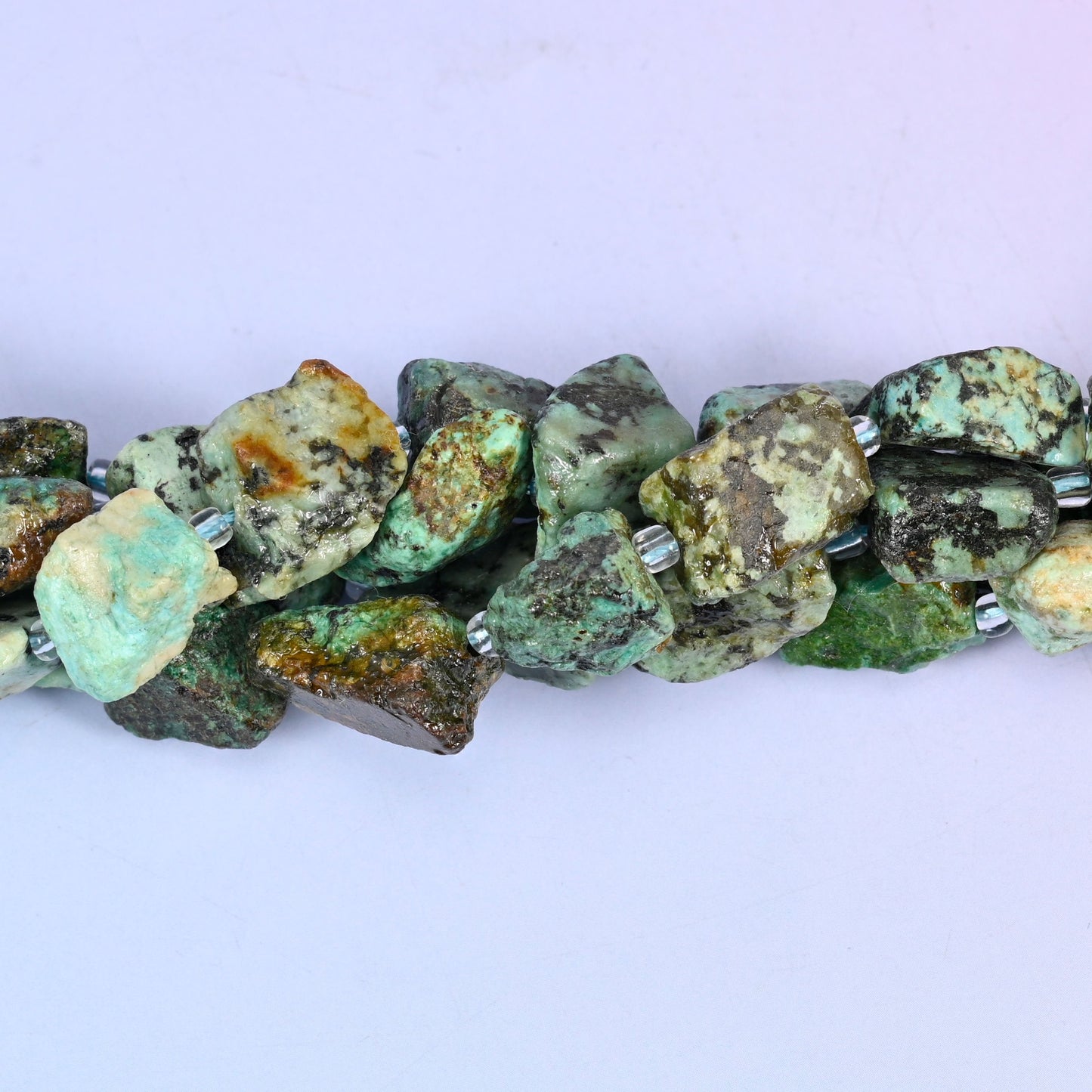 Raw, unpolished chunks with a rough quarry-cut surface, mottled seafoam and turquoise green broken up by heavy black and dark brown matrix veining, with the occasional pale cream or mustard patch.