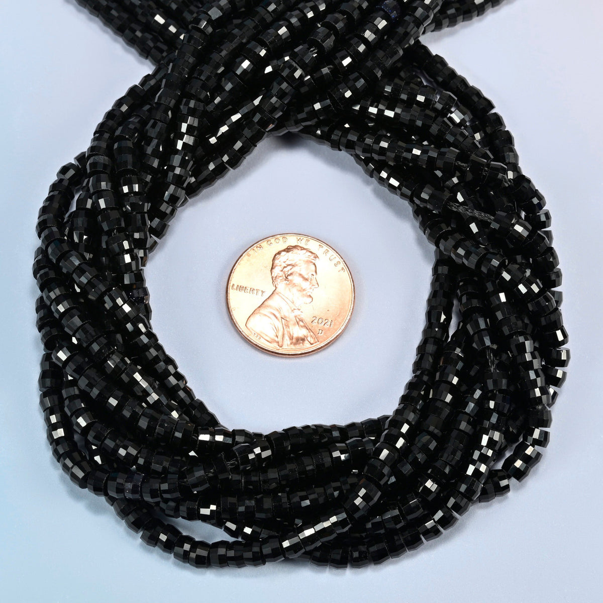 Black onyx faceted heishi disc beads 2x4mm coiled in a loop around a US penny for scale, close-up of the faceted disc shape