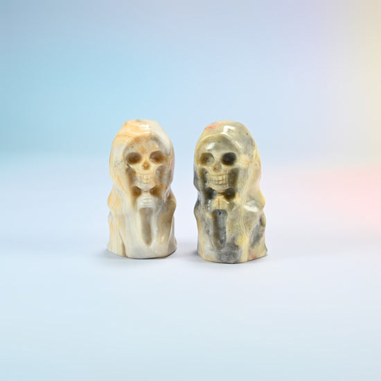 Two natural crazy agate hooded skull carvings, cream with gray-black patches, each one different