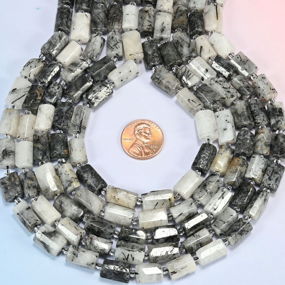 Black rutilated quartz faceted tube strands formed into a teardrop loop around a US penny for scale