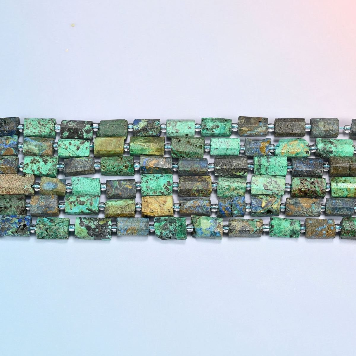 Four strands of azurite chrysocolla faceted tube beads laid in straight rows with clear seed bead spacers