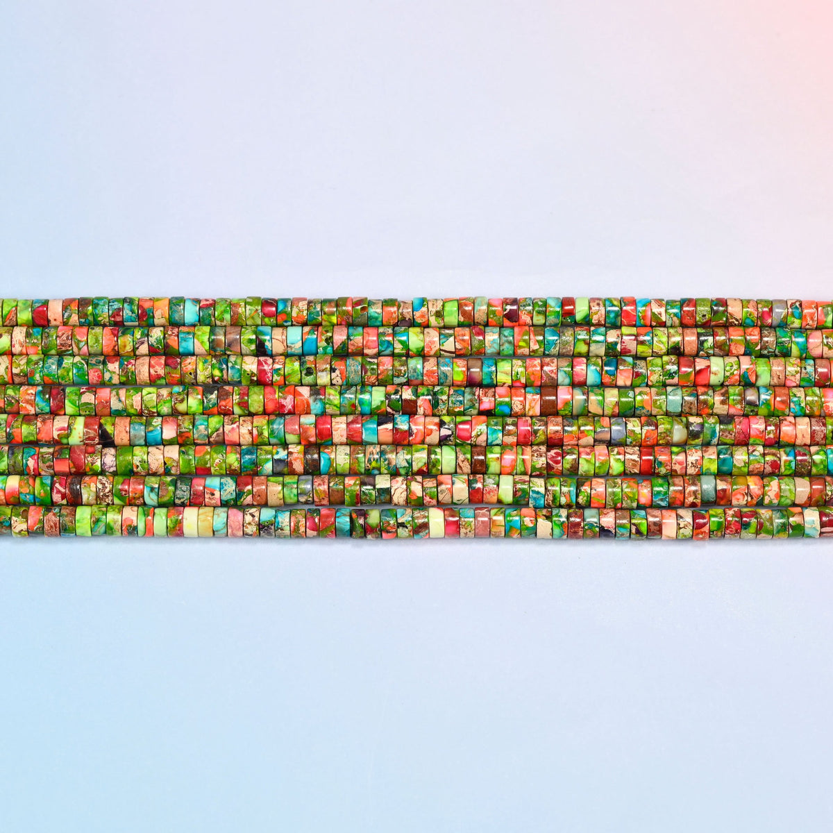 Several strands of dyed blue green sea sediment jasper heishi disc beads 2x4mm laid in straight rows, green and coral discs side by side