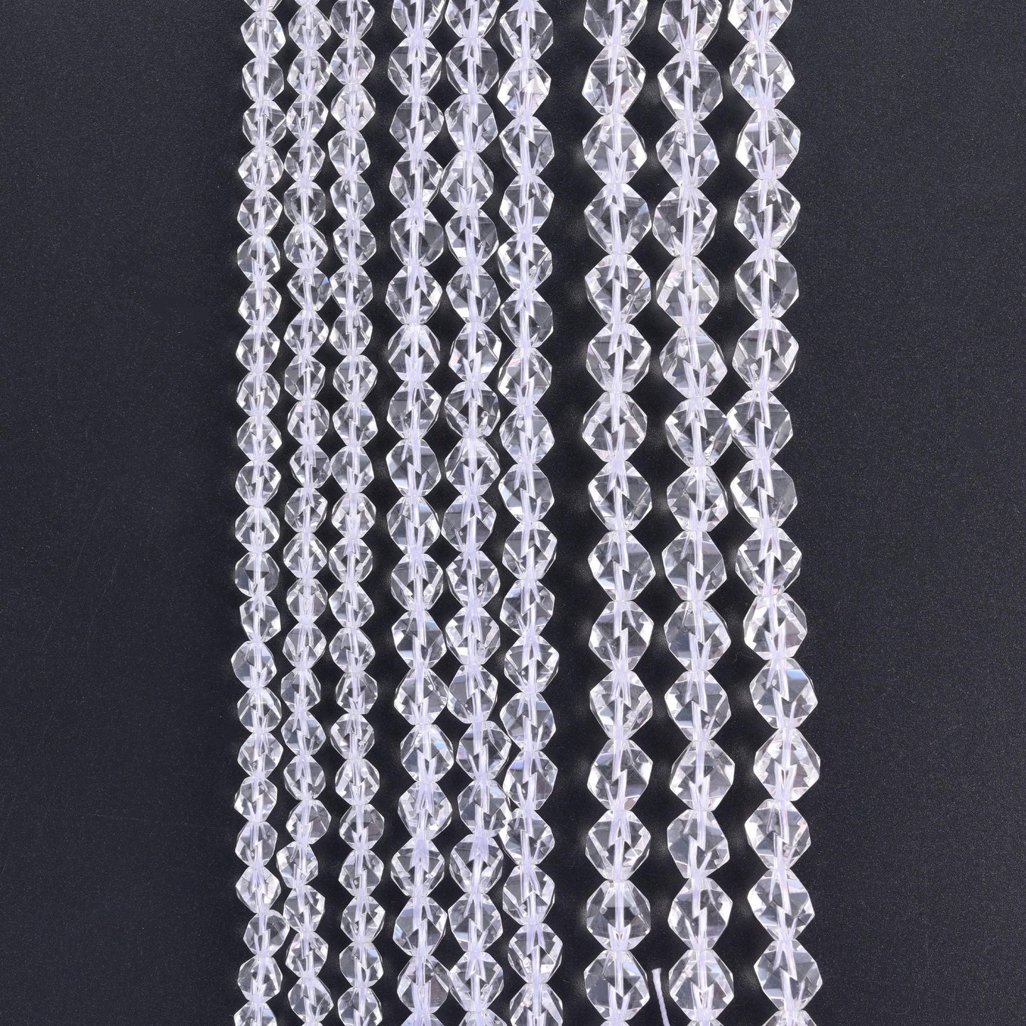 Clear Quartz diamond star cut beads, strands hanging vertically against a black background