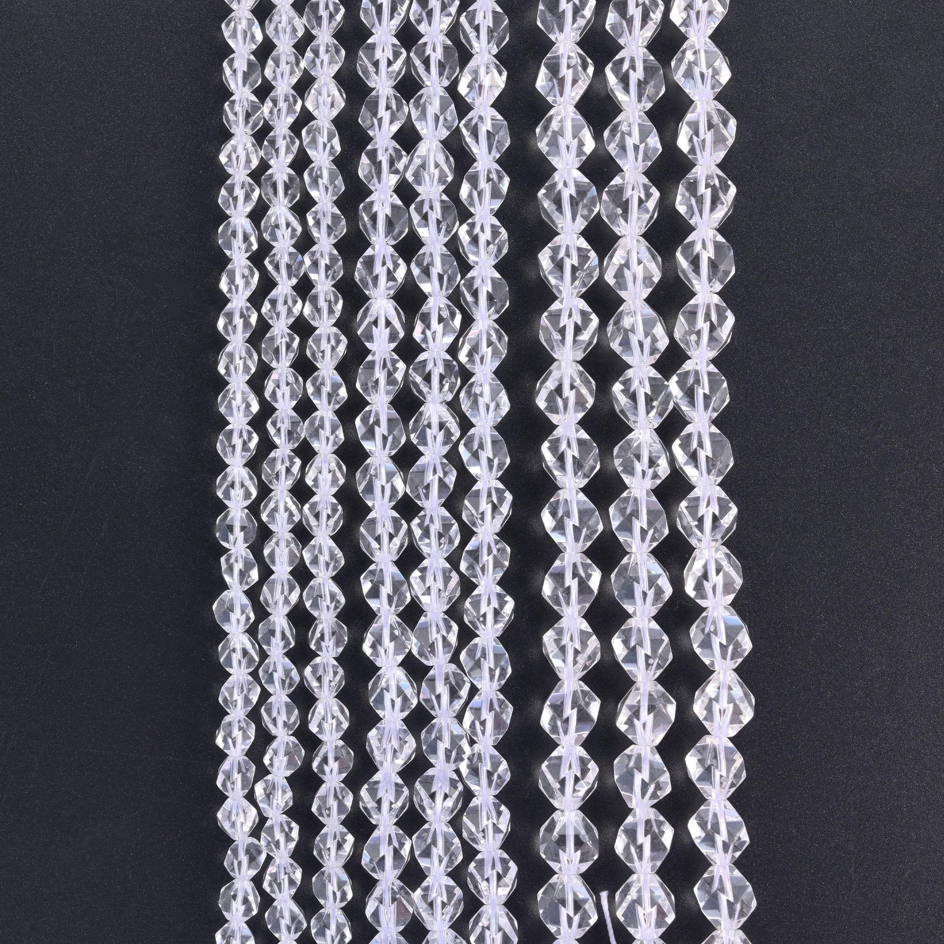 Clear Quartz diamond star cut beads, strands hanging vertically against a black background