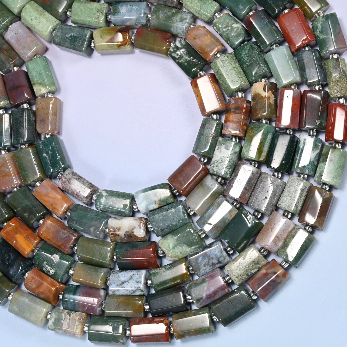 Circular coil of faceted Indian Agate tube bead strands on a lavender background with a penny in the center for size comparison.