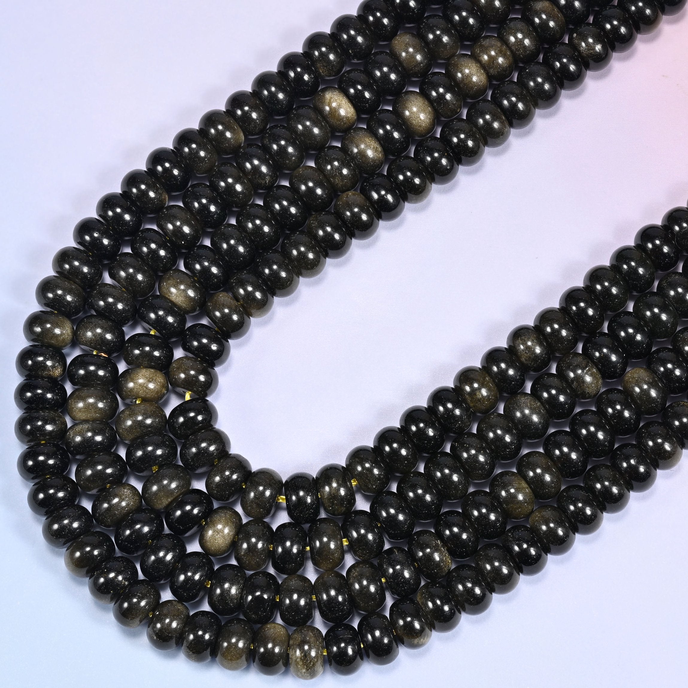 Close-up of Gold Obsidian rondelle beads coiled in a circular arrangement on a lavender background.