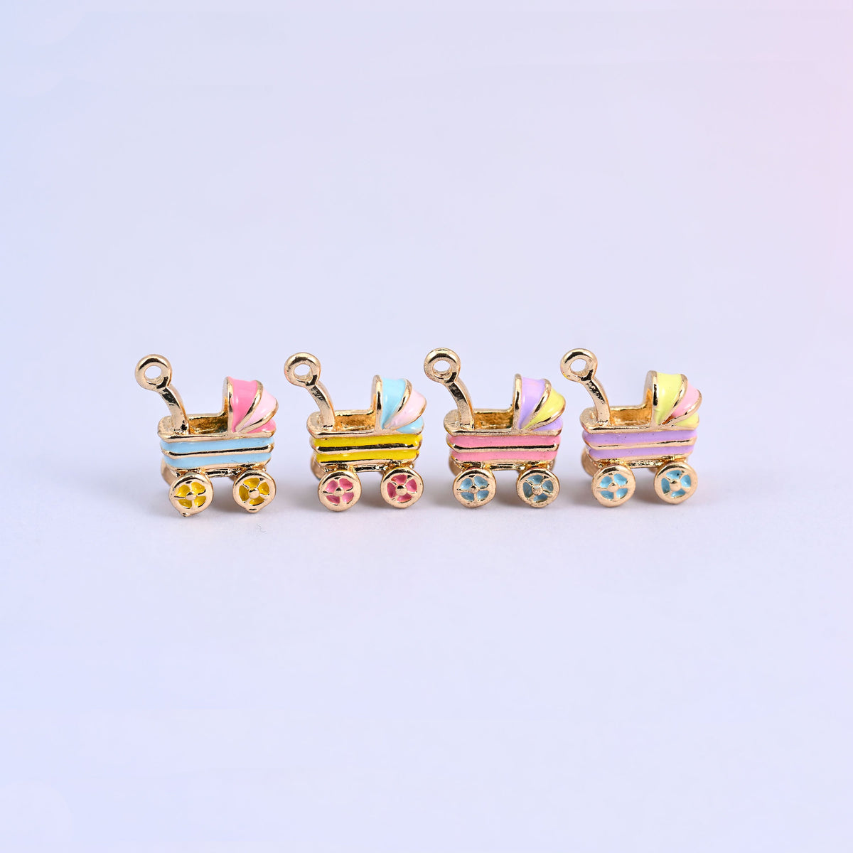 All four stroller charms in a row: light blue, yellow, pink and light purple enamel bodies.