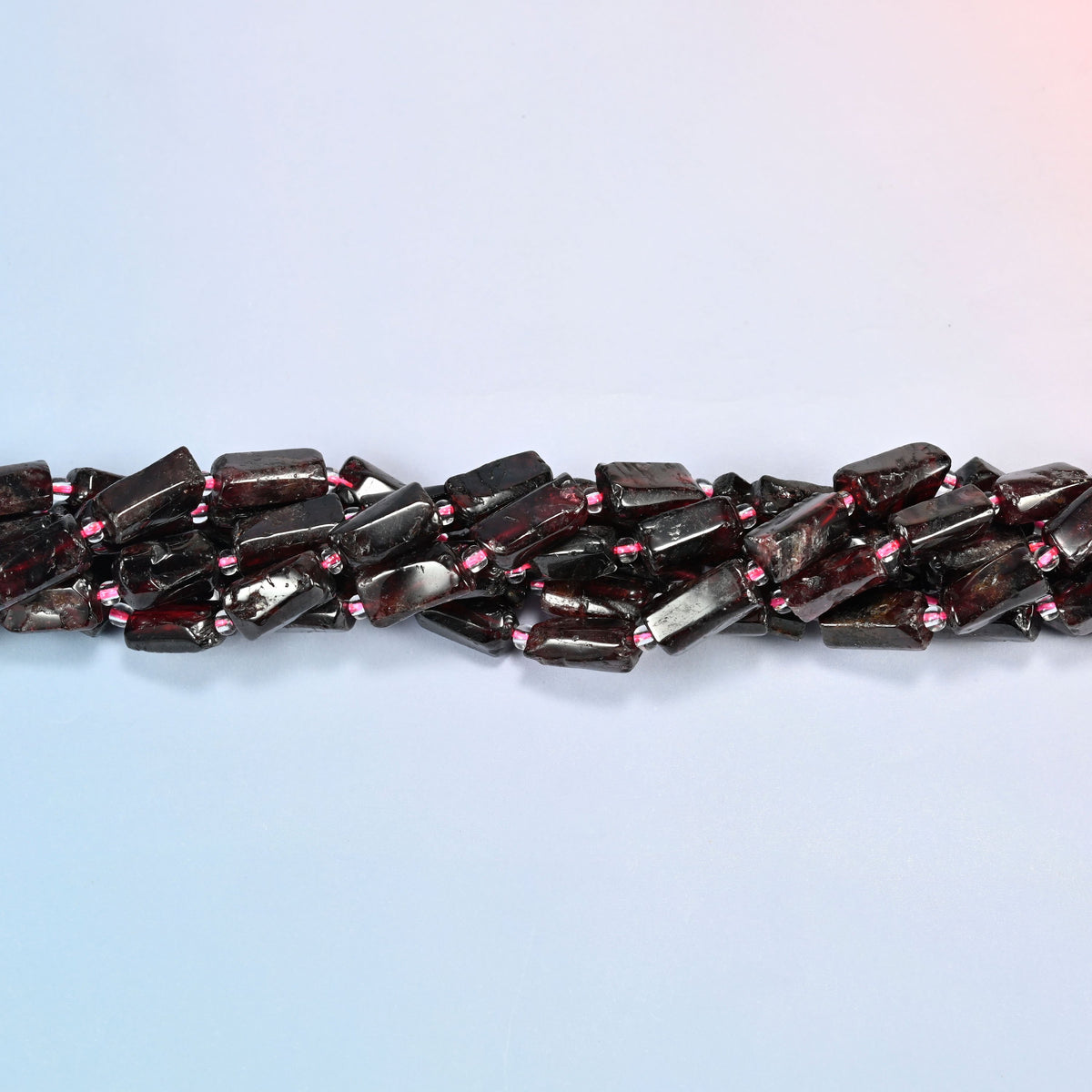 Strands of red garnet tube beads twisted together in a horizontal row