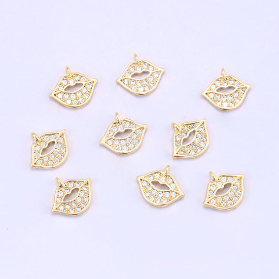 Small gold charms, nine gold plated lip charms with clear cubic zirconia scattered on a pale backdrop