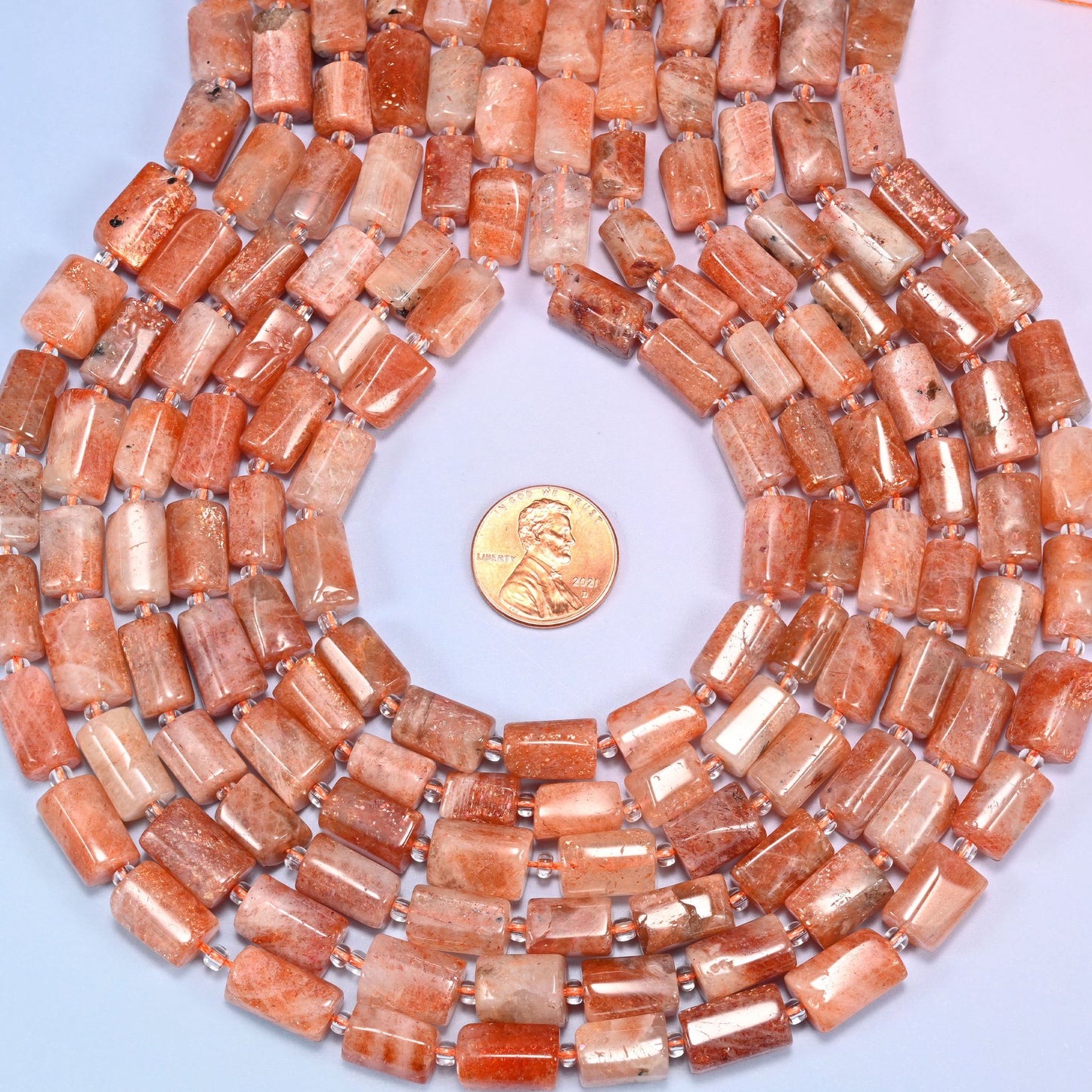 Circular coil of faceted Golden Strawberry Quartz tube bead strands on a lavender background with a penny in the center for size comparison.