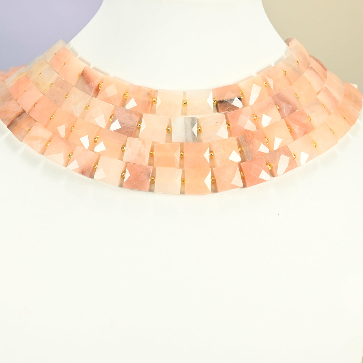 Natural pink aventurine faceted flat square strands arranged as a layered collar on a white display bust, peach pink beads across the neck