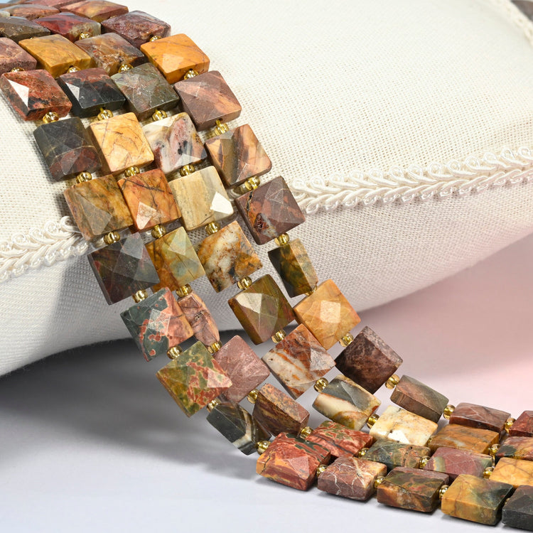 Natural red howlite faceted flat square beads 10x10mm with small gold seed bead spacers, several strands draped over a white cushion