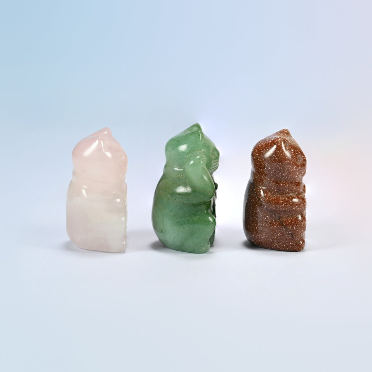 Side view of three gemstone fortune cat figurines showing the raised paw