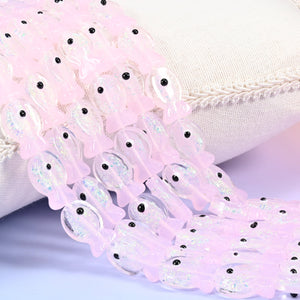 Iridescent pink fish glass bead strands spilling from a white linen cushion, each fish marked with a black eye dot