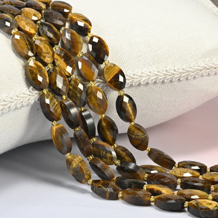 Tiger eye faceted flat oval beads 9x14mm with small gold seed bead spacers, several strands draped over a white cushion