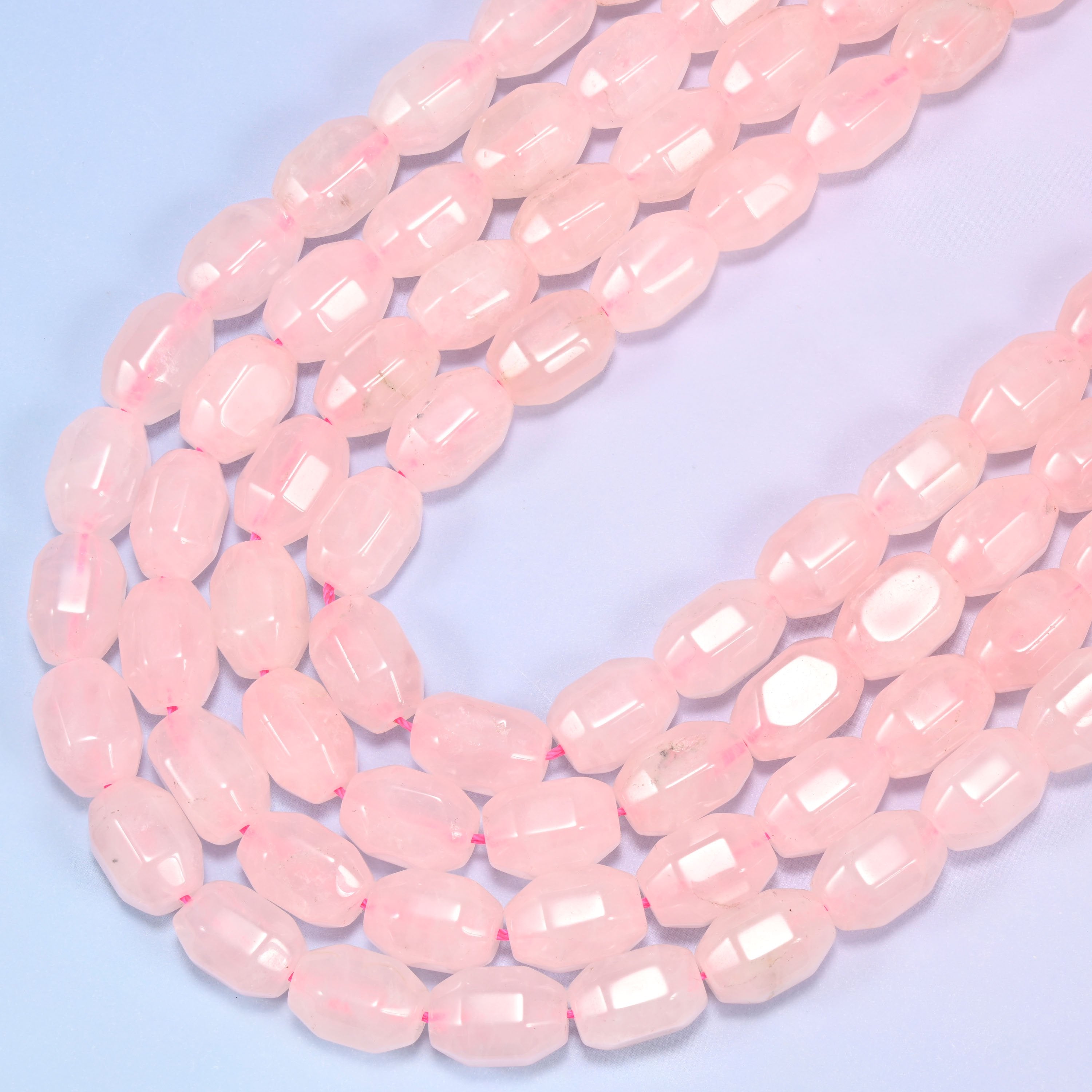 Close-up of a circular coil of Rose Quartz faceted barrel beads on a light blue background.