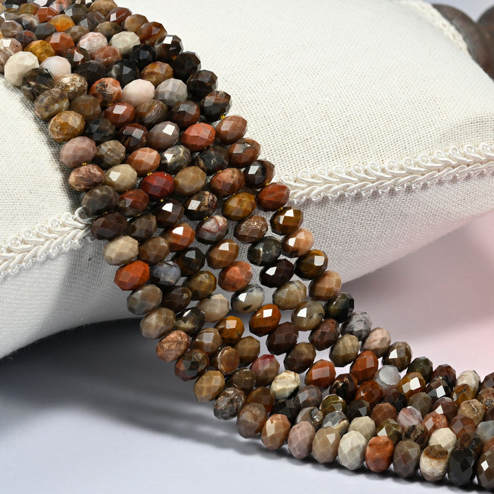 Petrified wood faceted rondelle beads 5x8mm in brown, red-brown, gray and cream, several strands draped over a white cushion