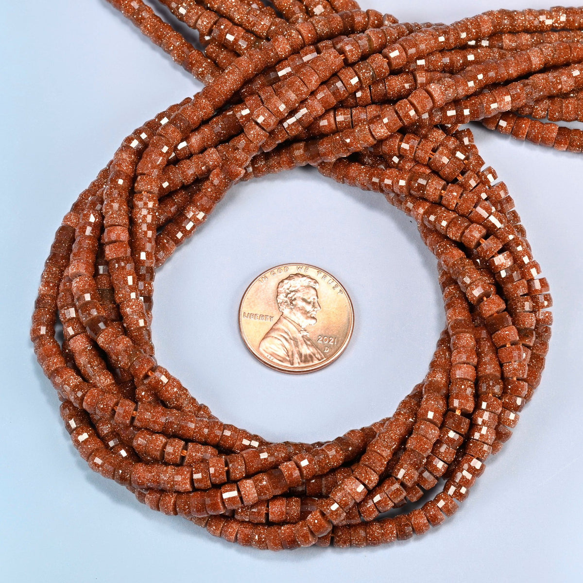 Gold sandstone faceted heishi disc beads 2x4mm coiled in a loop around a US penny for scale, close-up of the faceted disc shape
