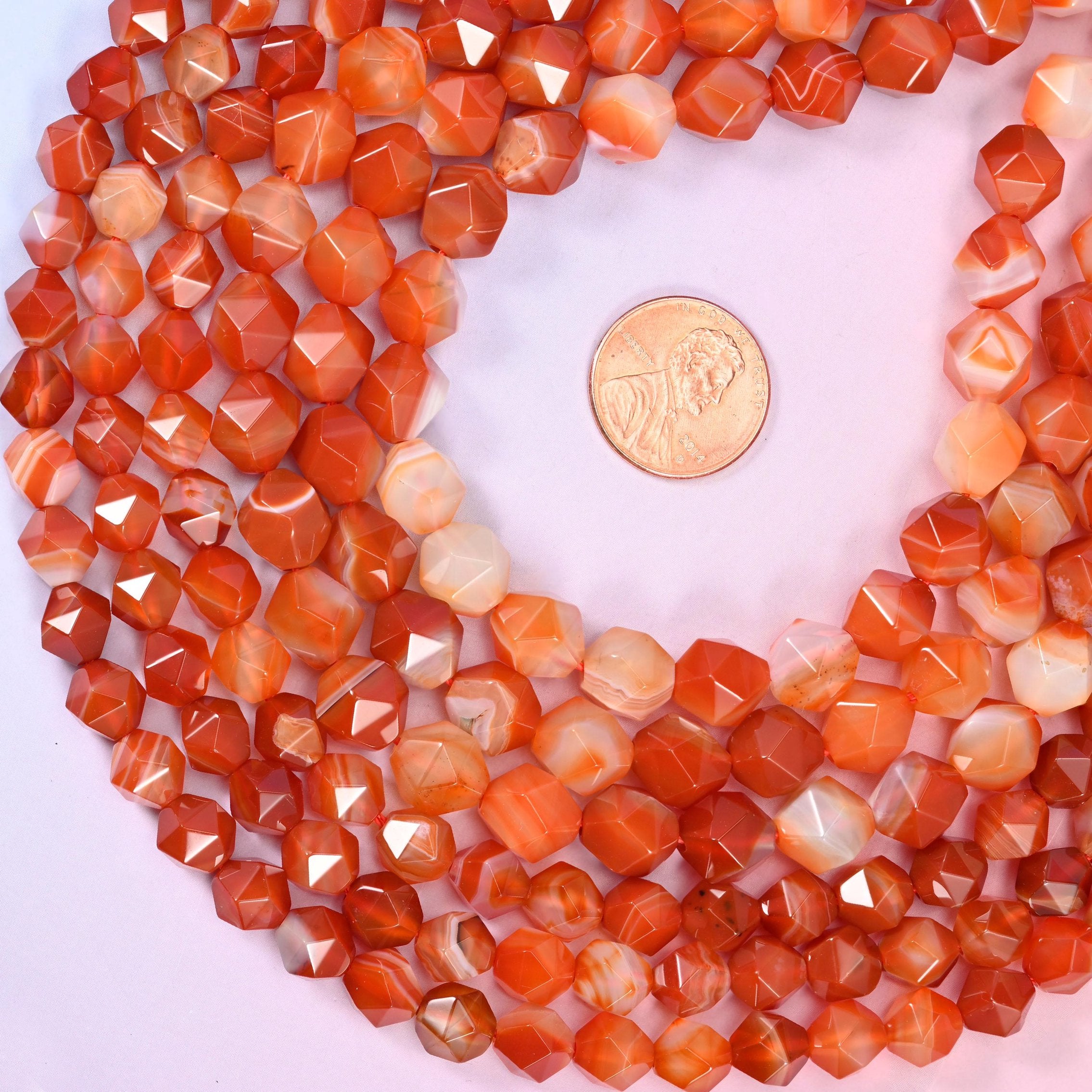 Dyed Red Stripe Agate diamond star cut beads coiled around a US penny for size reference, centre drilled with a polished faceted finish