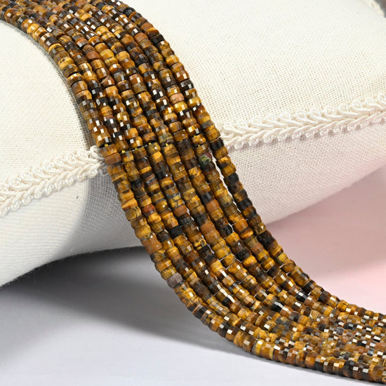 Tiger eye faceted heishi disc beads 2x4mm, several strands draped over a white cushion