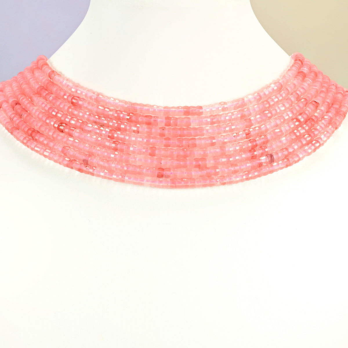 Melon quartz faceted heishi disc strands arranged as a layered collar on a white display bust, pink beads across the neck