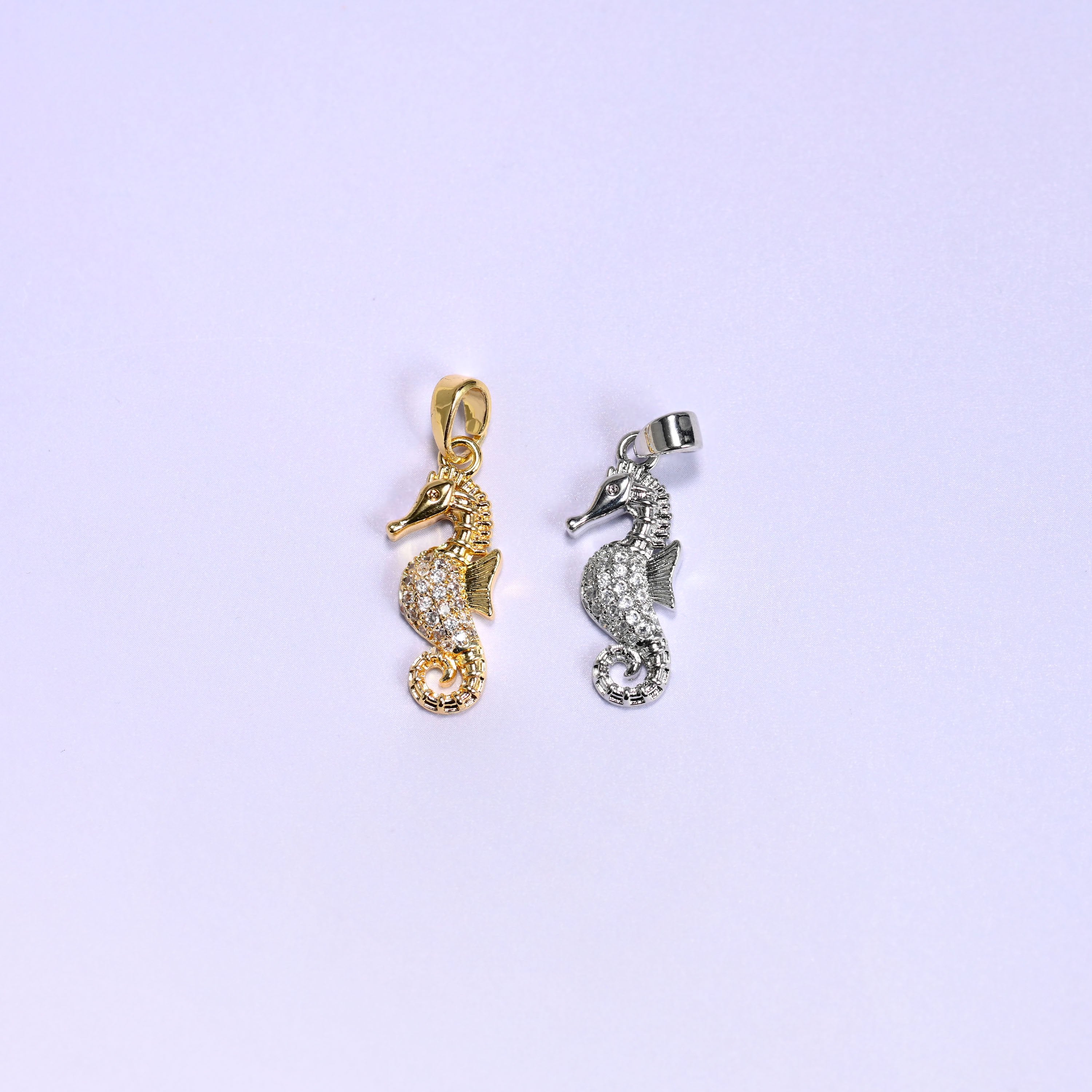 Sea horse zirconia pendant colour comparison, the 18K gold plated charm beside the platinum tone version, both paved with clear zirconia on a lavender backdrop.
