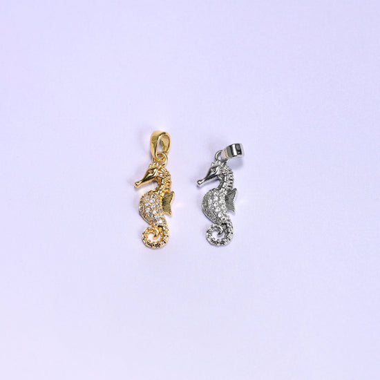 Sea horse zirconia pendant colour comparison, the 18K gold plated charm beside the platinum tone version, both paved with clear zirconia on a lavender backdrop.