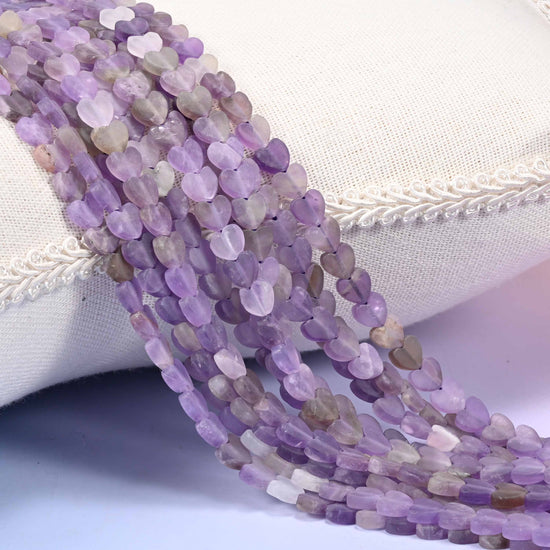 Full 15 inch strand of purple and lavender amethyst flat heart-shaped beads, 6mm matte beads, 15 inch strand, draped on a display cushion