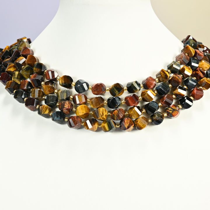 Tricolor tiger eye faceted spiral twist strands arranged as a layered collar on a white display bust, gold, red and blue-gray beads across the neck