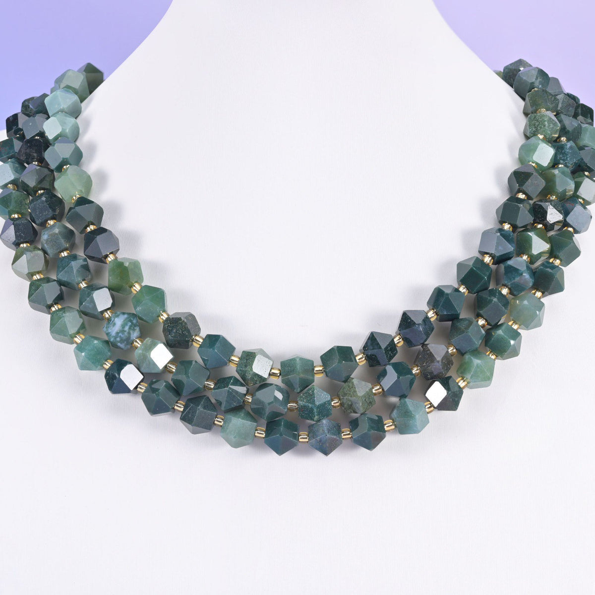 Faceted 8 sides diamond rhombus beads in moss agate on a white neck display, three strands layered.