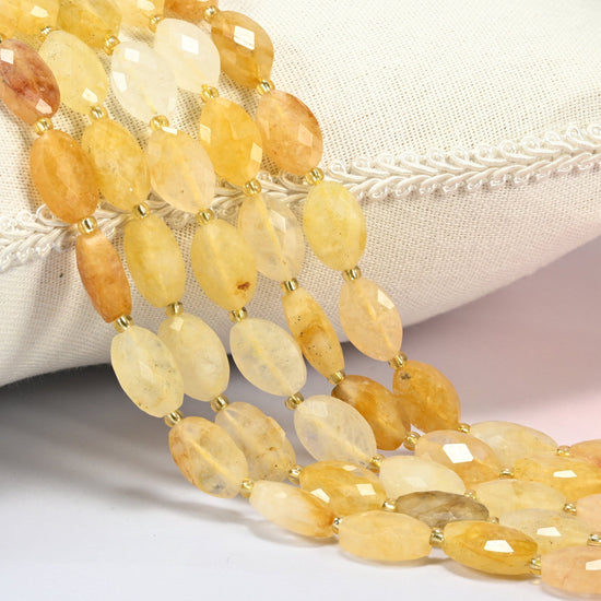 Golden healer quartz faceted flat oval beads 9x14mm with small gold seed bead spacers, several strands draped over a white cushion