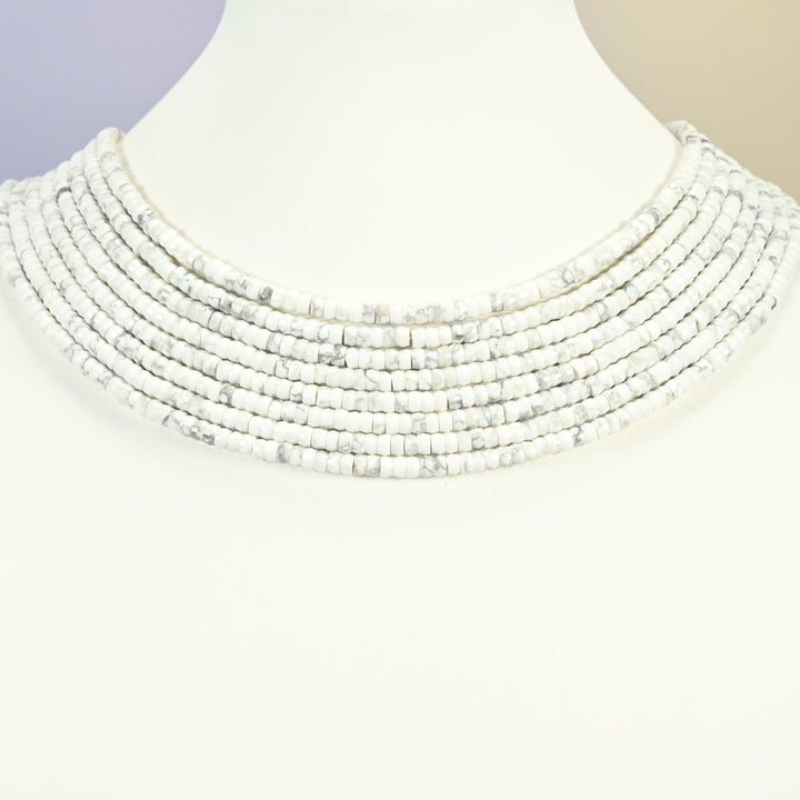 White howlite faceted heishi disc strands arranged as a layered collar on a white display bust, white beads across the neck