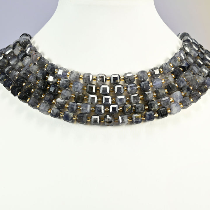 Iolite faceted cube strands arranged as a layered collar on a white display bust, blue-gray and navy beads across the neck