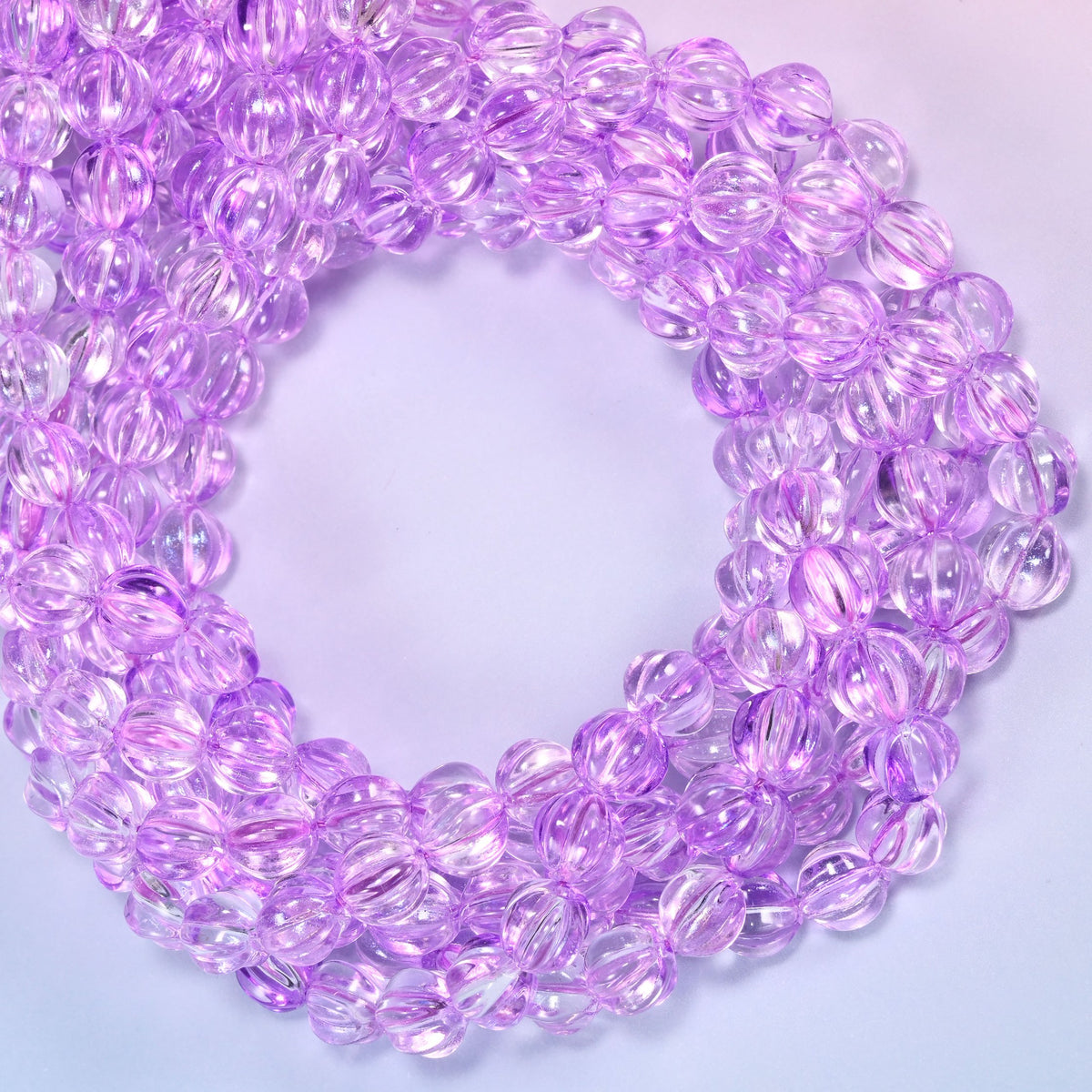 Clear purple pumpkin glass beads coiled with the open center to one side, showing the fluted grooves end on.