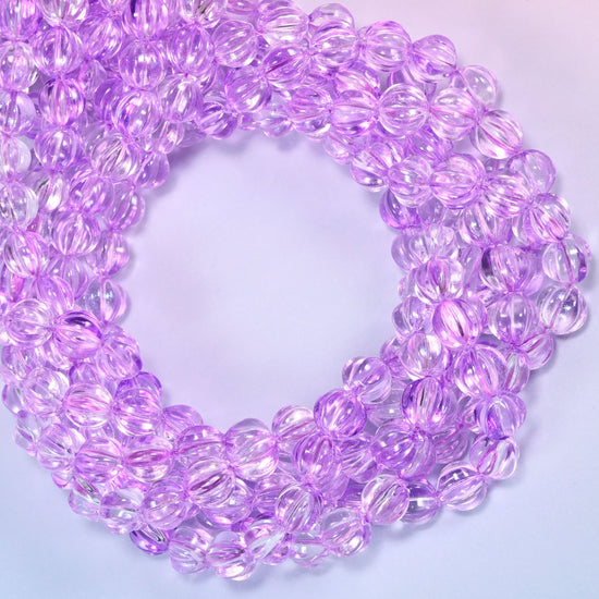 Clear purple pumpkin glass beads coiled with the open center to one side, showing the fluted grooves end on.