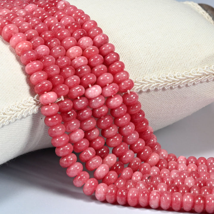 Raspberry Red dyed jade gemstone rondelle beads draped over a cushion in soft rows, a deep rosy raspberry red with a glossy polish