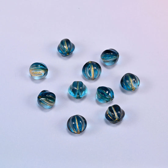 A scattered group of loose 8mm dark blue gold pumpkin glass beads, showing the melon ribs and the drill holes.