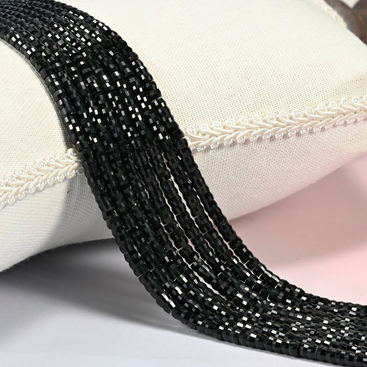 Black onyx faceted heishi disc beads 2x4mm, several strands draped over a white cushion