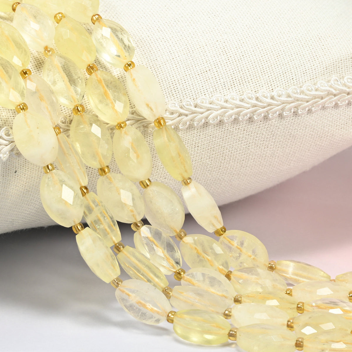Citrine faceted flat oval beads 9x14mm with small gold seed bead spacers, several strands draped over a white cushion