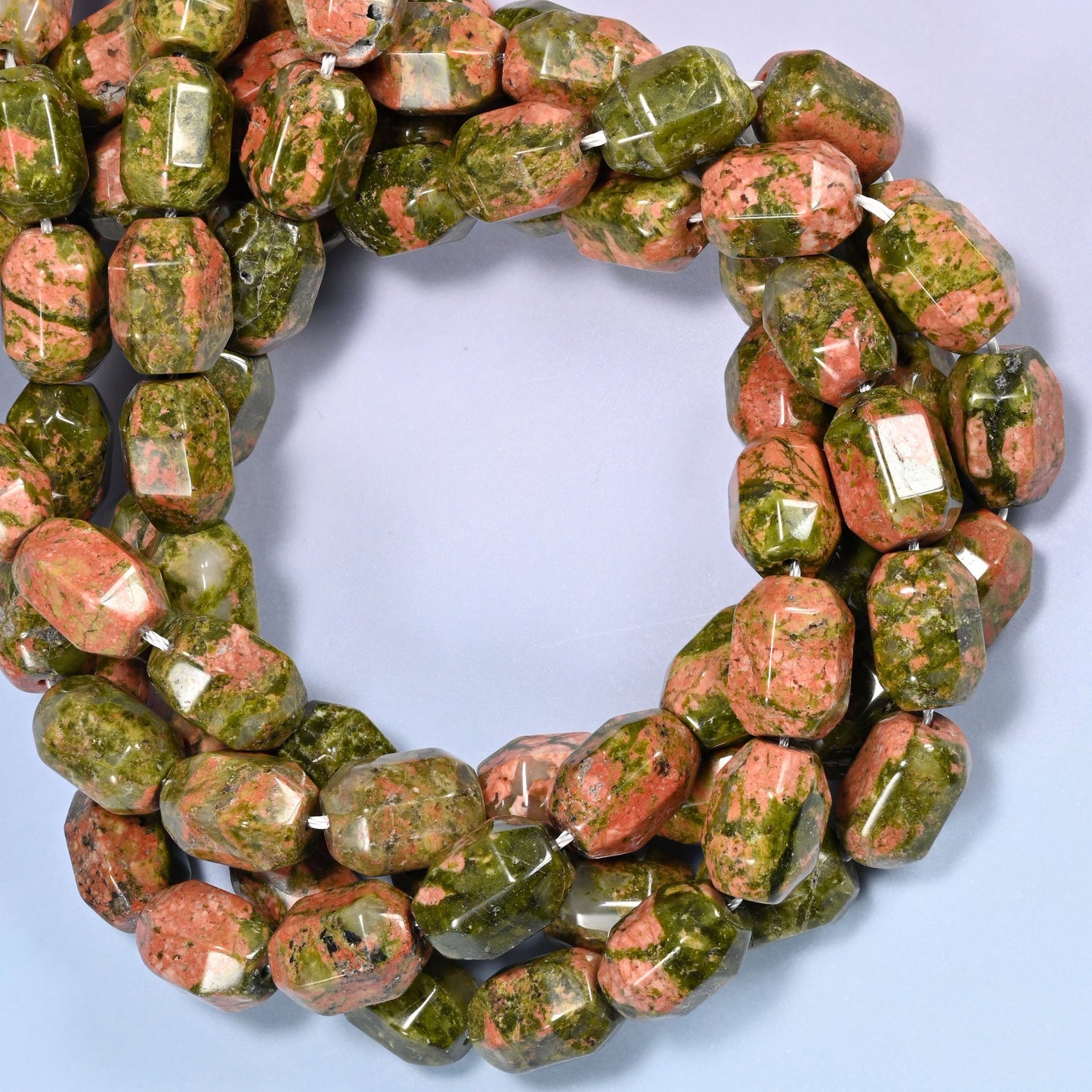 Close-up circular coil of faceted Unakite barrel beads, showing the green and salmon color mix.
